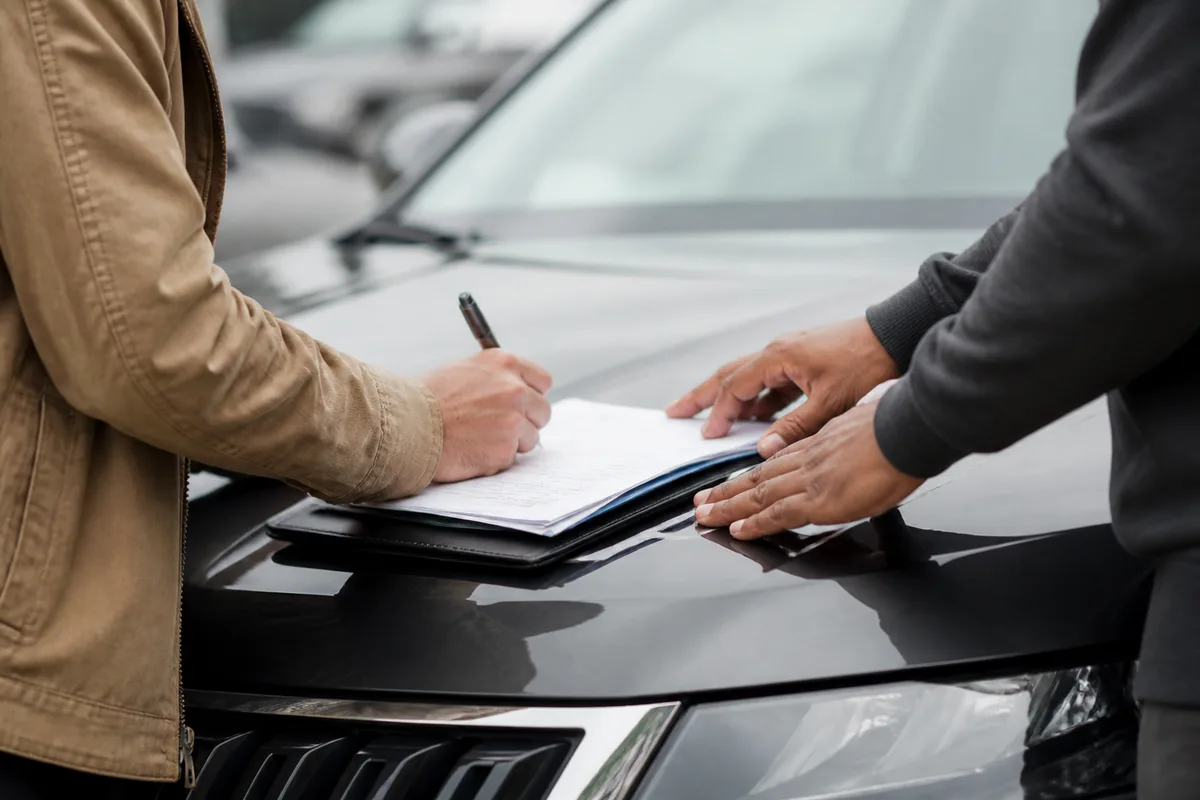 Deux personnes signant des papiers de vente sur le capot d&rsquo;une voiture