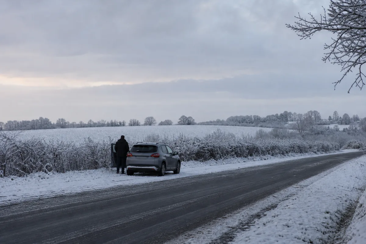 Voiture arrêtée sur un bas-côté enneigé au bord d’une route de campagne