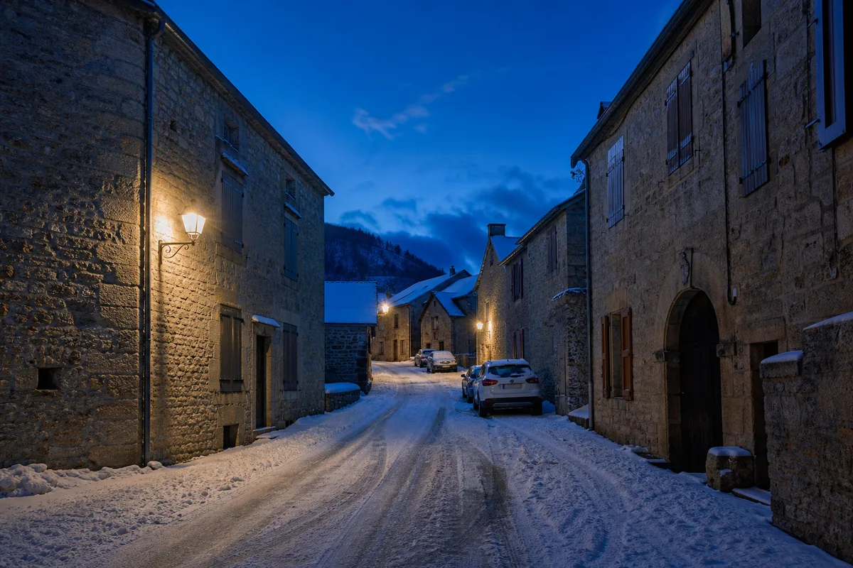 Rue de village de montagne enneigée avec voitures garées en fin de journée